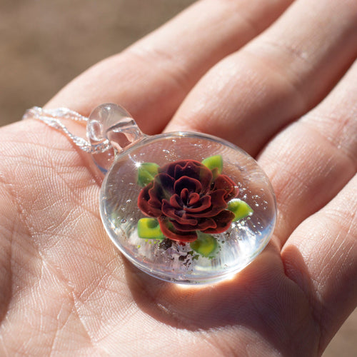 A glass pendant with a red rose inside and cremation ashes